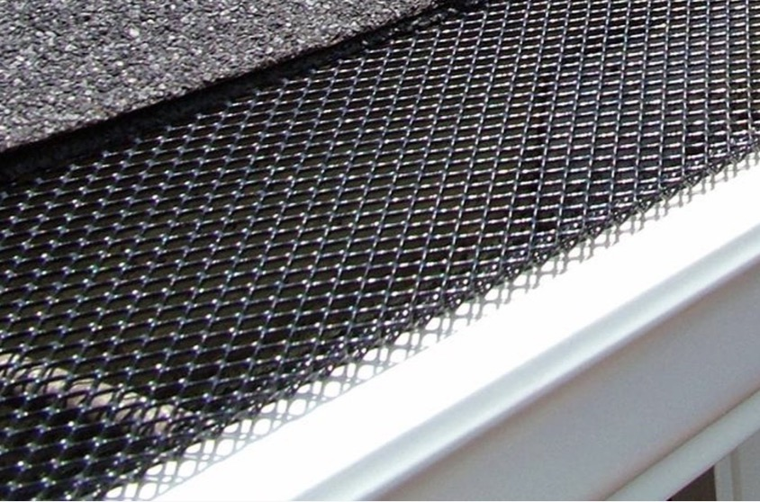 Black coated mesh leaf guard installed under shingles on a white gutter