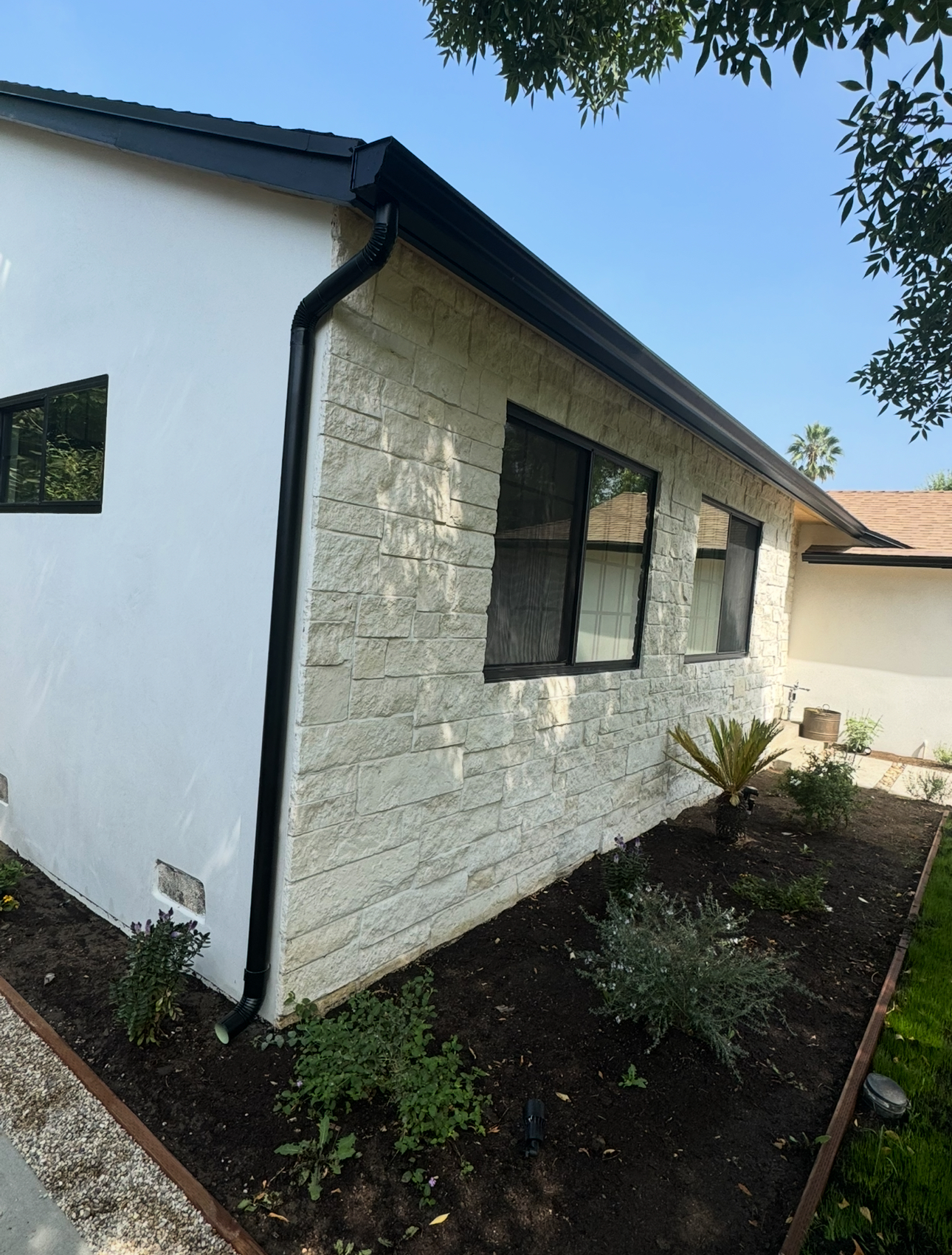 Black seamless gutter and downspout on a stone-front home