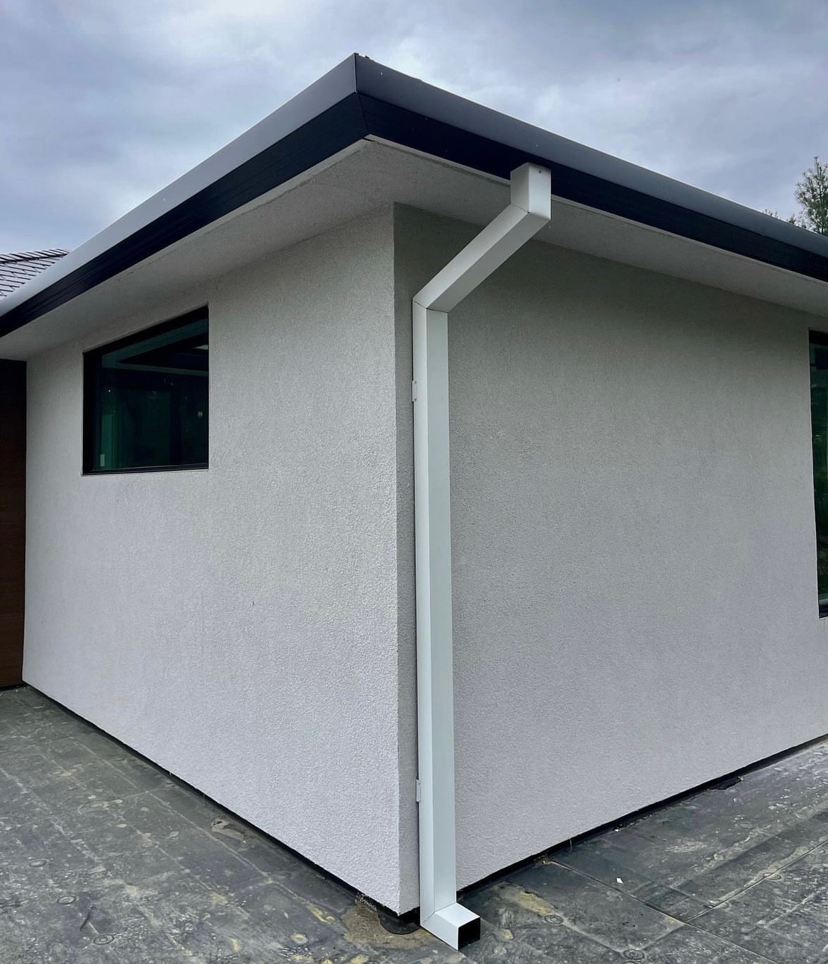 Black gutter with white downspout on a modern home corner